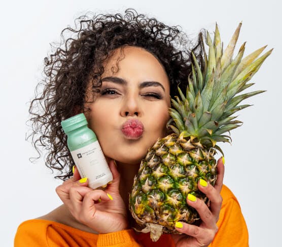 Na zdjęciu znajduję się jeden z kadrów sesji zdjęciowej wykonanej dla marki Collibre. Obrazek przedstawia twarz pięknej kobiety w kręconych włosach, która w swojej dłoni trzyma kolagen i ananasa. Owoc symbolizuje smak kolagenu.
