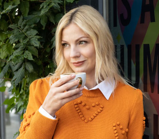 Na zdjęciu znajduje się jedna z realizacji Influencer Marketingu - kadr z sesji zdjęciowej z Katarzyną Kołeczek. Modelka romantycznie patrzy przed siebie, w dłoni trzyma filiżankę z kawą.